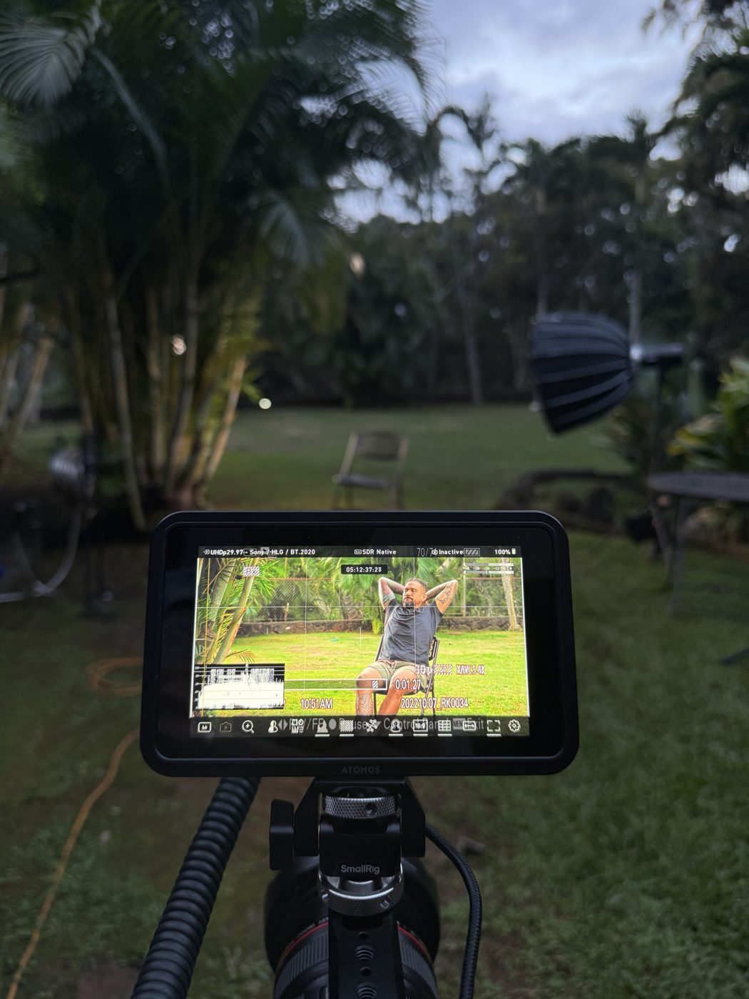 Behind the scenes: an Atomos monitor on the camera rig shows Yancy framed for the backyard interview, with a softbox in the background at dusk